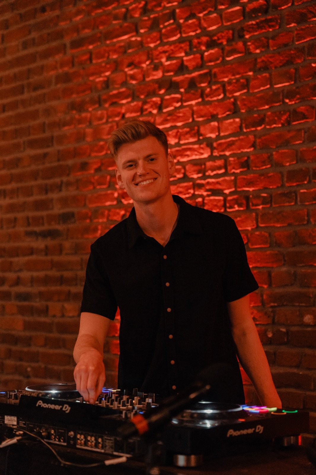 Porträt von DJ Tim Matthiä lächelnd vor roter Backsteinwand