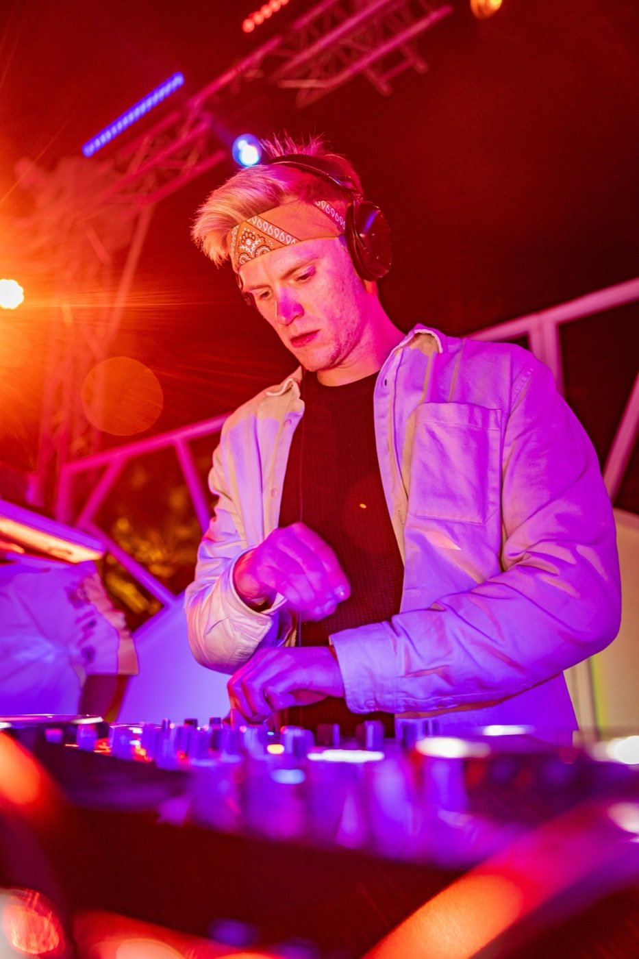 DJ Tim Matthiä mit Kopfhörern und Bandana am Mischpult in violettem Bühnenlicht