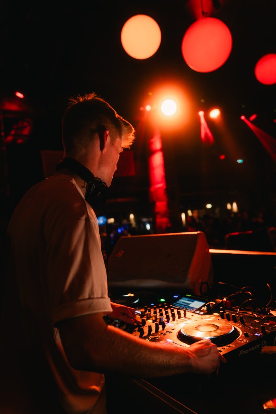 DJ Tim Matthiä von hinten am DJ-Pult vor roten Scheinwerfern