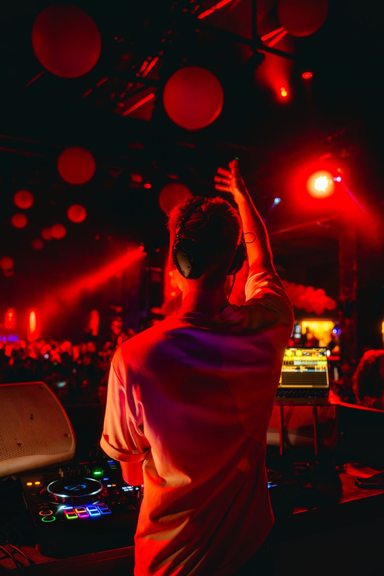 DJ Tim Matthiä mit erhobenem Arm am DJ-Pult in der Halle Tor 2, umgeben von warmem rotem Bühnenlicht